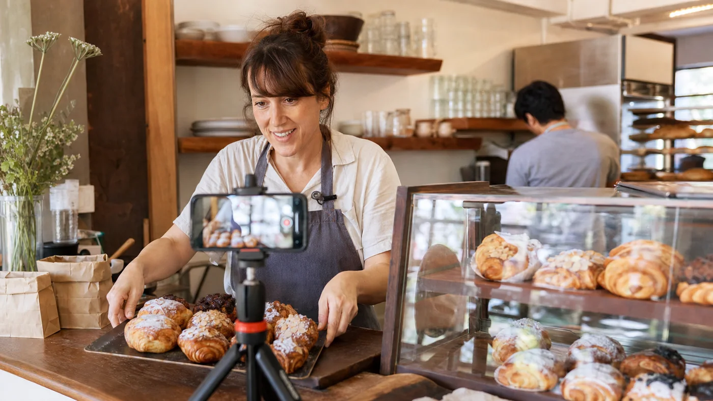 Un petit boulanger enregistrant du contenu produit avec un smartphone en travaillant dans sa boutique