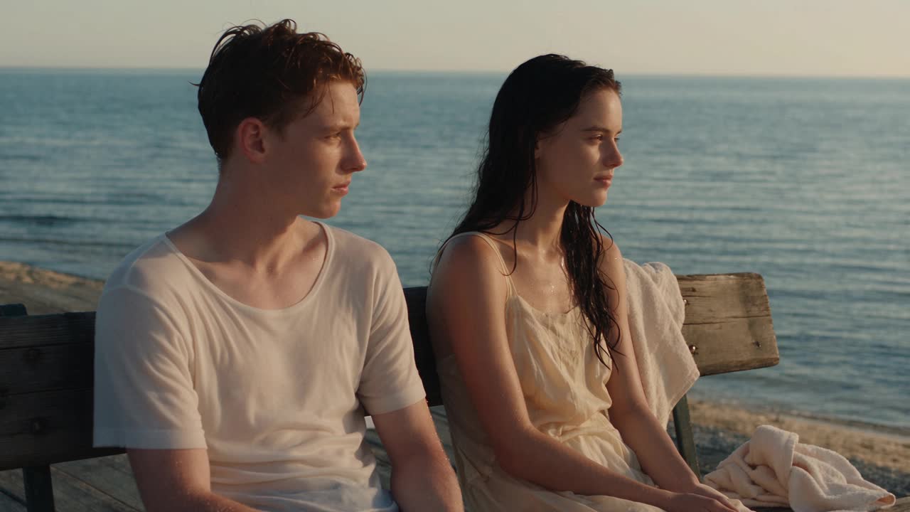 A natural-light cinematic scene of two people seated beside the sea