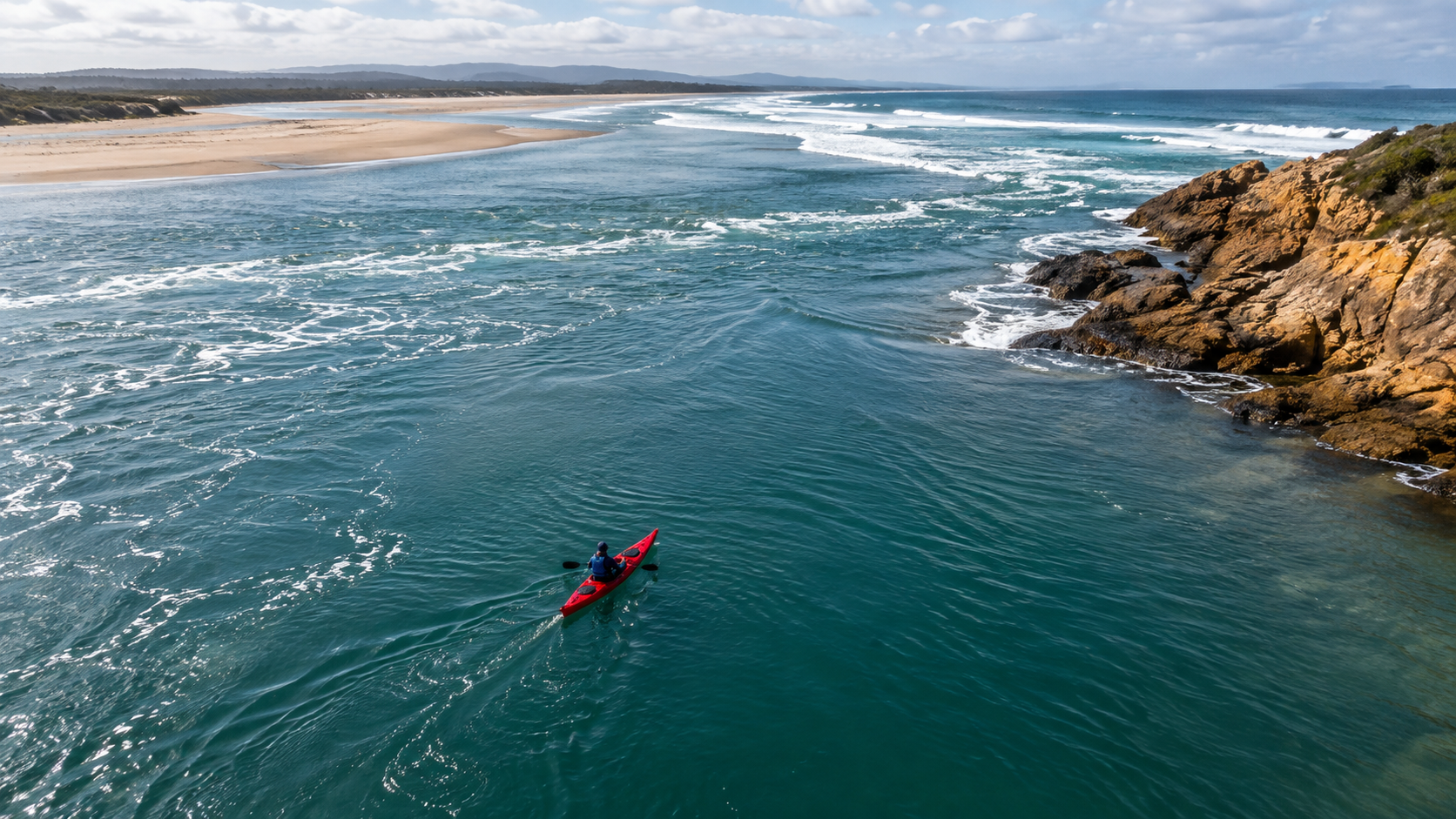 Un kayak rouge à l’embouchure large d’une rivière, à côté d’une côte rocheuse